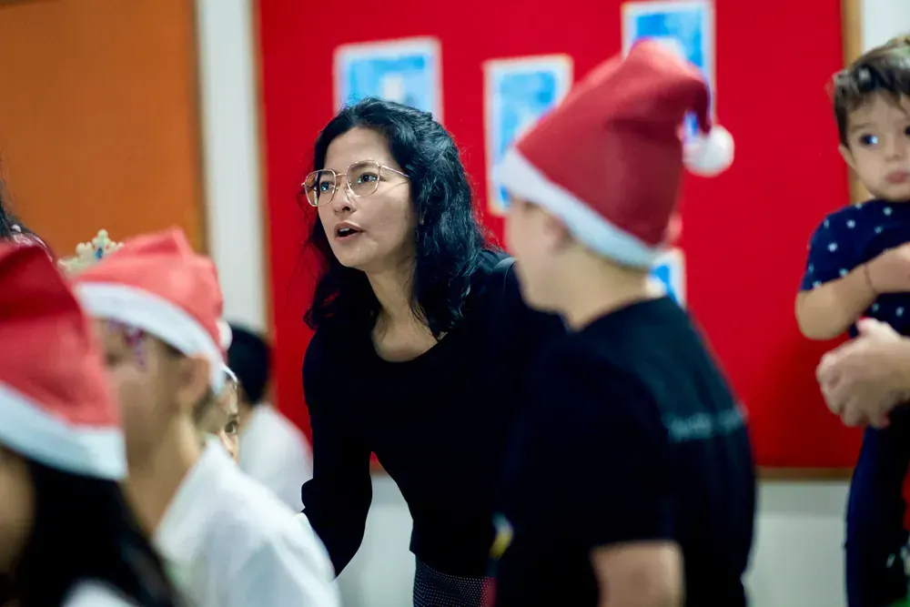 A woman is talking to a group of children wearing santa hats.