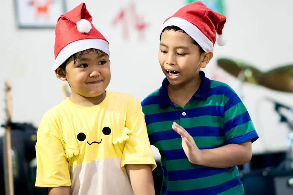 Two young boys wearing santa hats are standing next to each other.