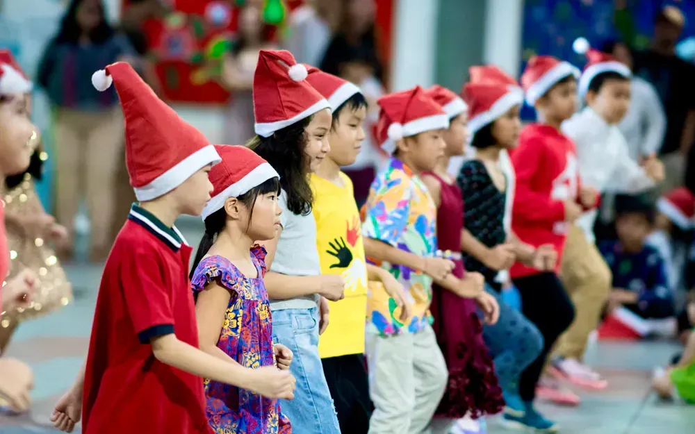 A group of children wearing santa hats are dancing together.