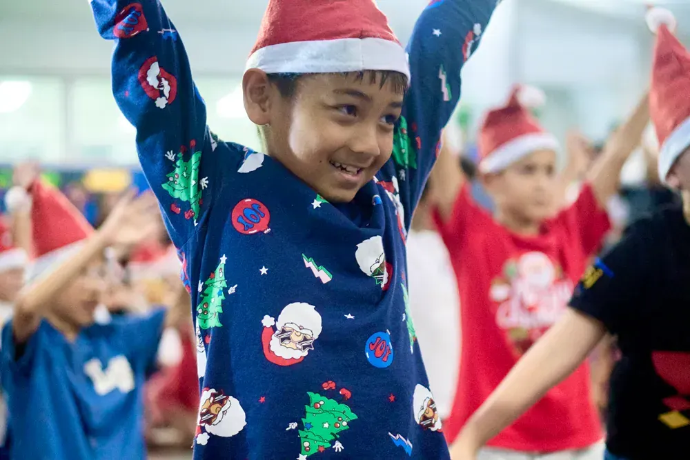 A group of children wearing santa hats are dancing together.