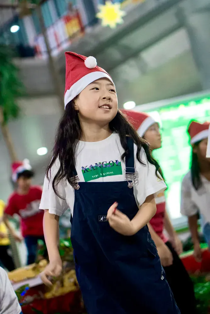 A little girl is wearing a santa hat and overalls.