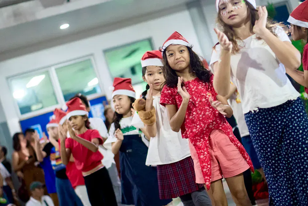 A group of young girls wearing santa hats are dancing together.