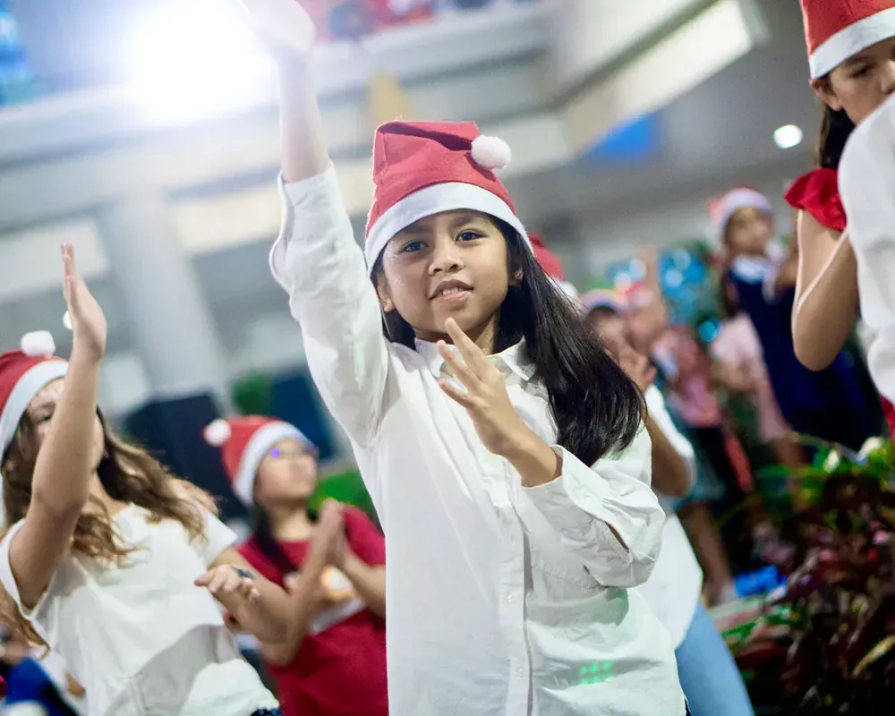 A group of children wearing santa hats are dancing together.