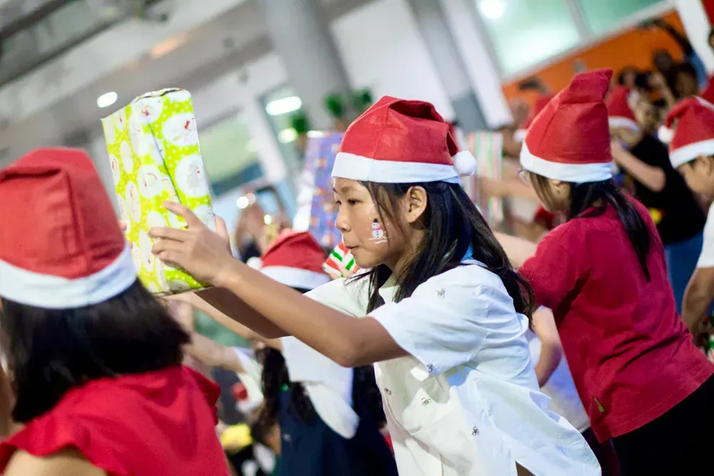 A group of children wearing santa hats are holding christmas presents.