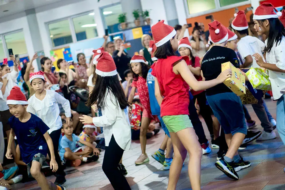 A group of children wearing santa hats are dancing in a room.