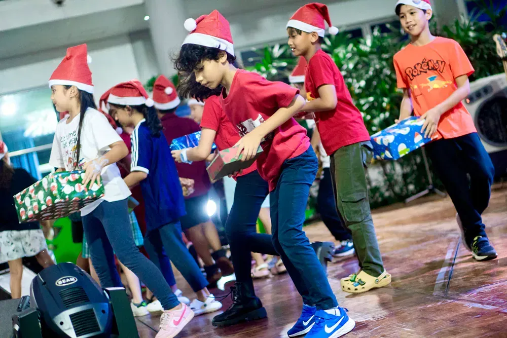 A group of children wearing santa hats are dancing on a stage.