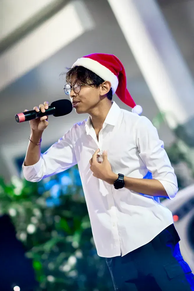 A young man wearing a santa hat is singing into a microphone.