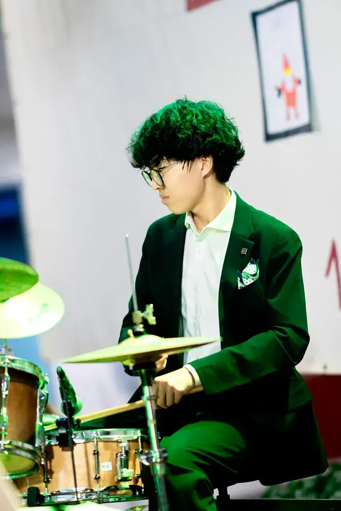 A man in a green suit is playing drums.