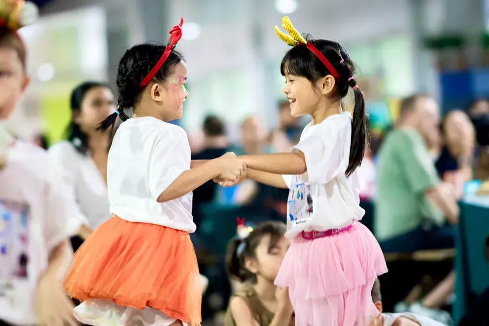 Two little girls are shaking hands in front of a crowd at a party.