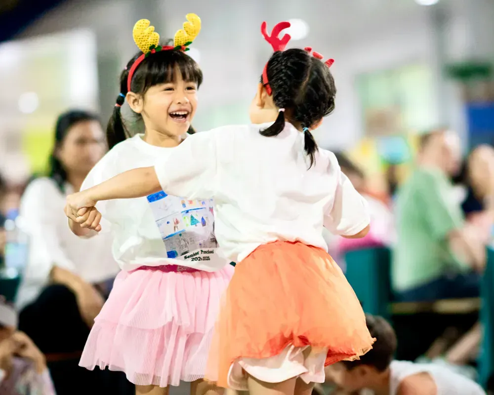 Two little girls are dancing together in front of a crowd.