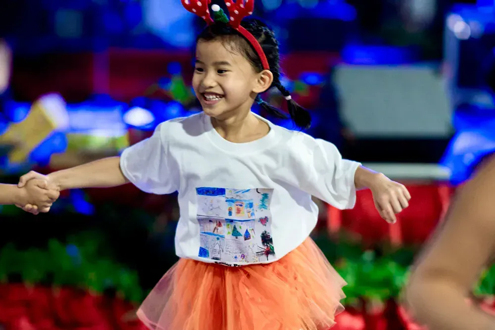A little girl wearing a minnie mouse headband and an orange tutu is holding hands with another child.