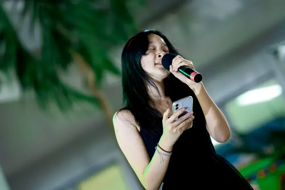 A woman is singing into a microphone while holding a cell phone.