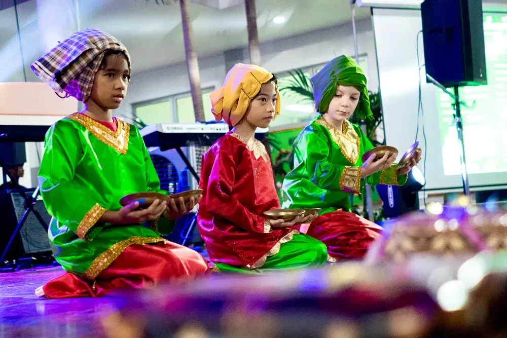 A group of children in traditional costumes are sitting on the floor holding bowls.
