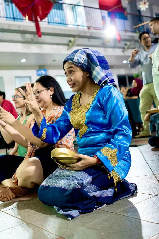 A woman in a blue dress is kneeling down on the floor playing a drum.
