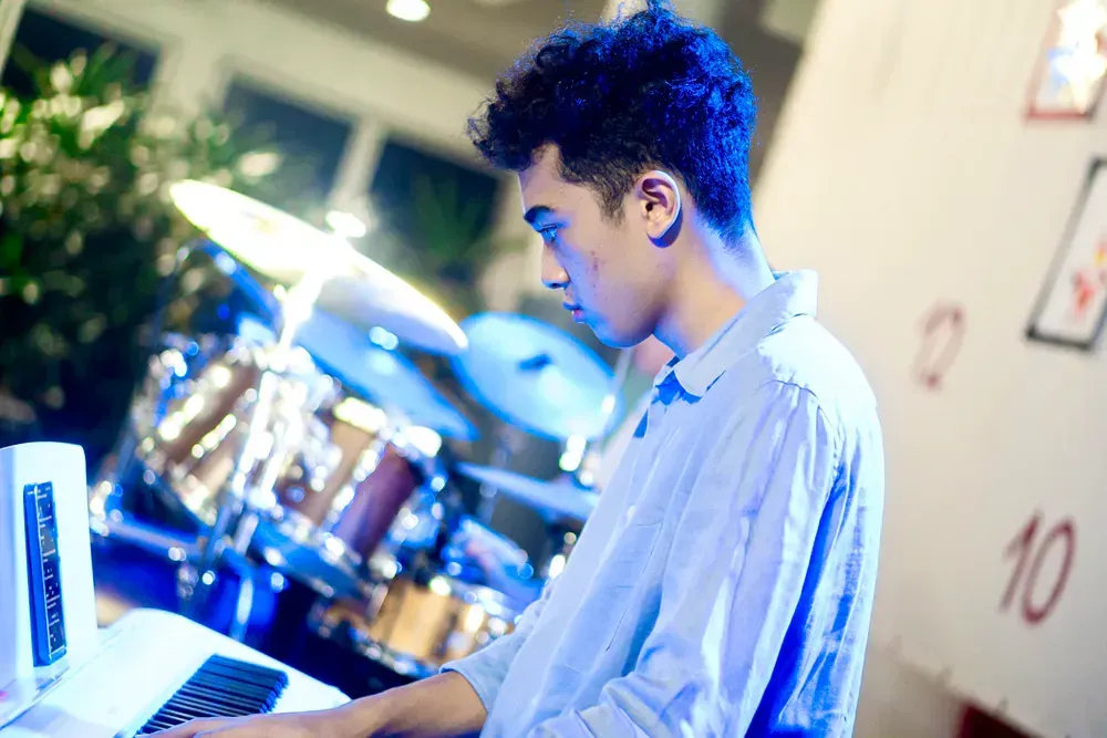 A man is using a laptop in front of a drum set.