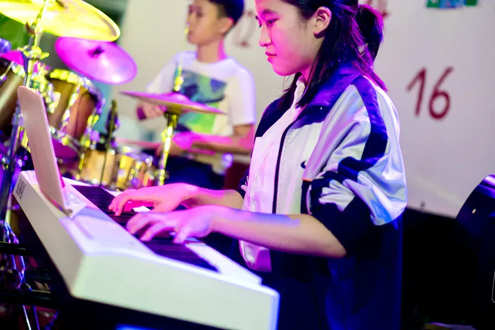 A girl is playing a keyboard in front of a drum set.