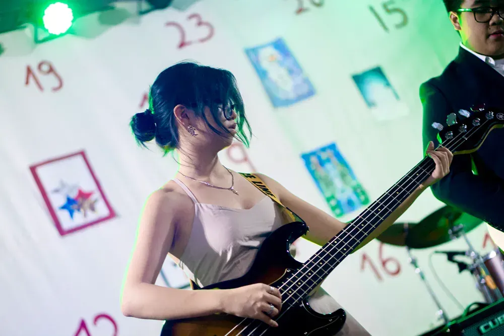A woman is playing a bass guitar in front of a calendar