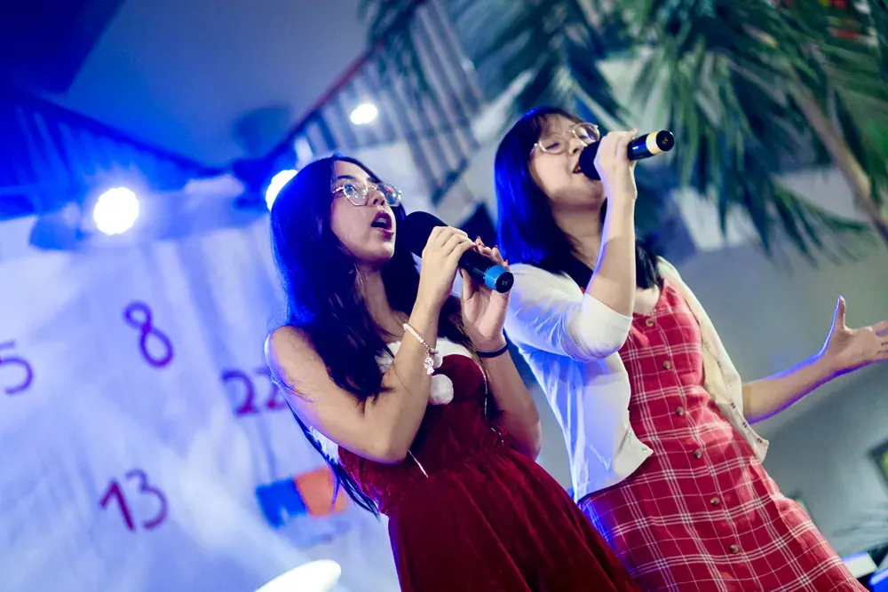 Two girls are singing into microphones on a stage.