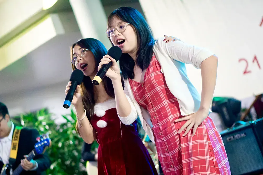 Two girls are singing into microphones while standing next to each other.