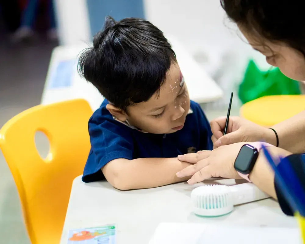 A woman is helping a young boy with his homework at a table.
