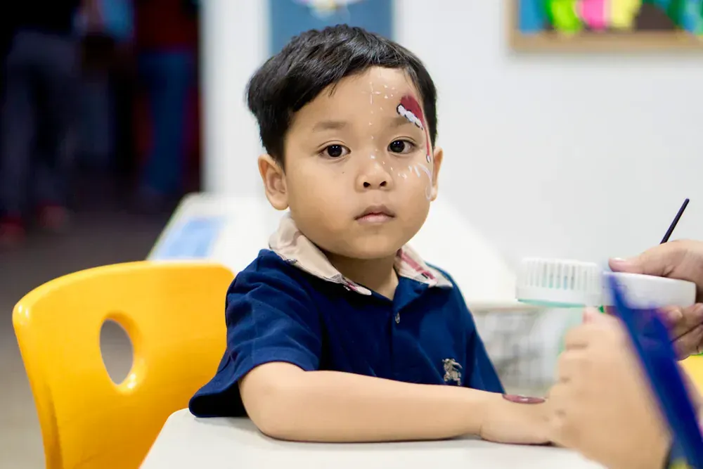 A young boy is sitting at a table with his face painted.