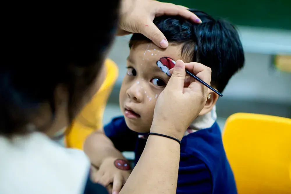 A little boy is getting his face painted by a woman.