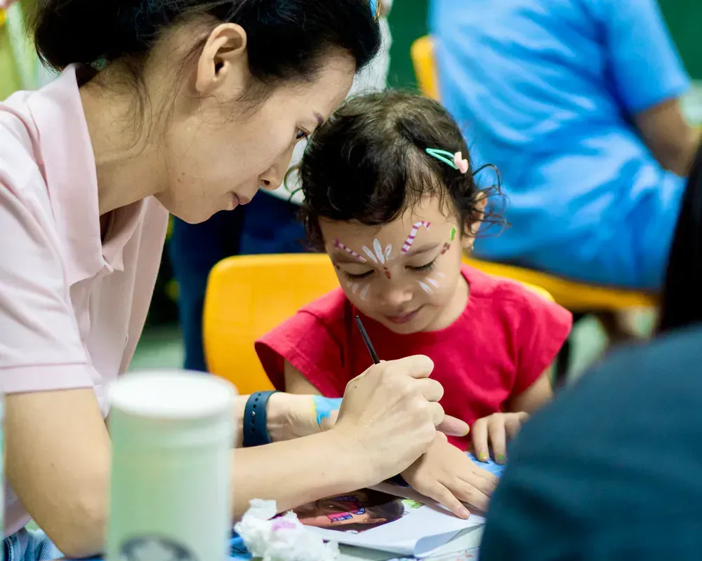 A woman is helping a little girl with her face paint