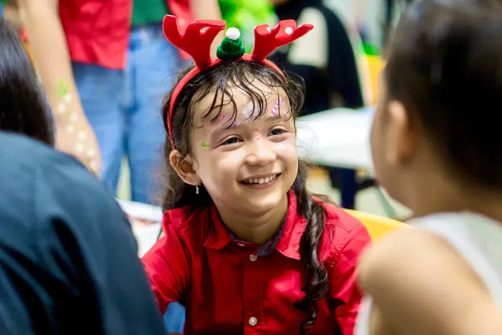 A little girl is wearing a reindeer headband and smiling.