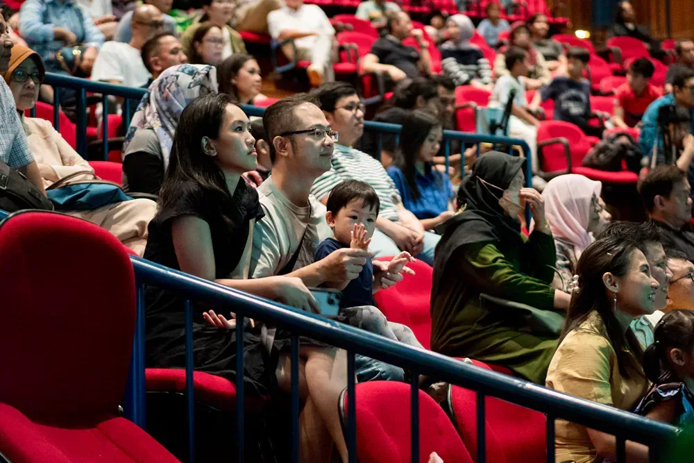 A crowd of people are sitting in red seats in a theater.