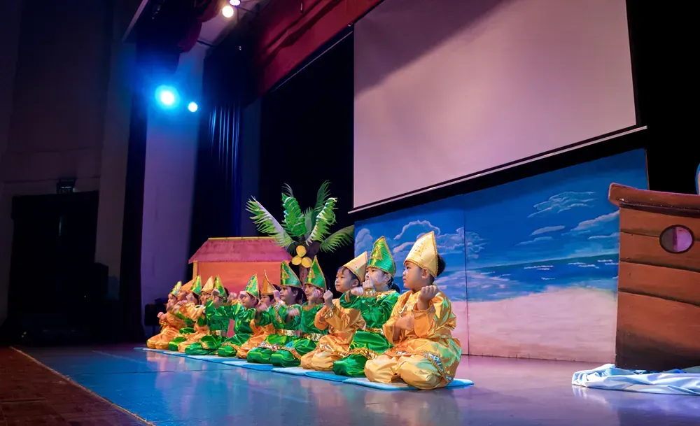 A group of people sitting on a stage with a boat in the background