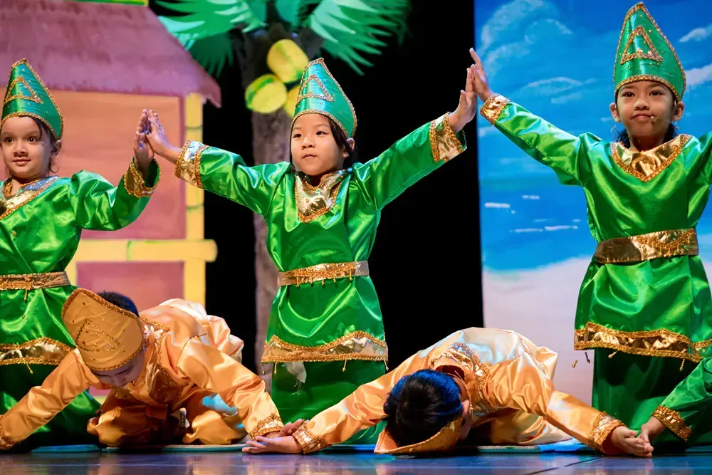A group of children in green and gold costumes are dancing on a stage.