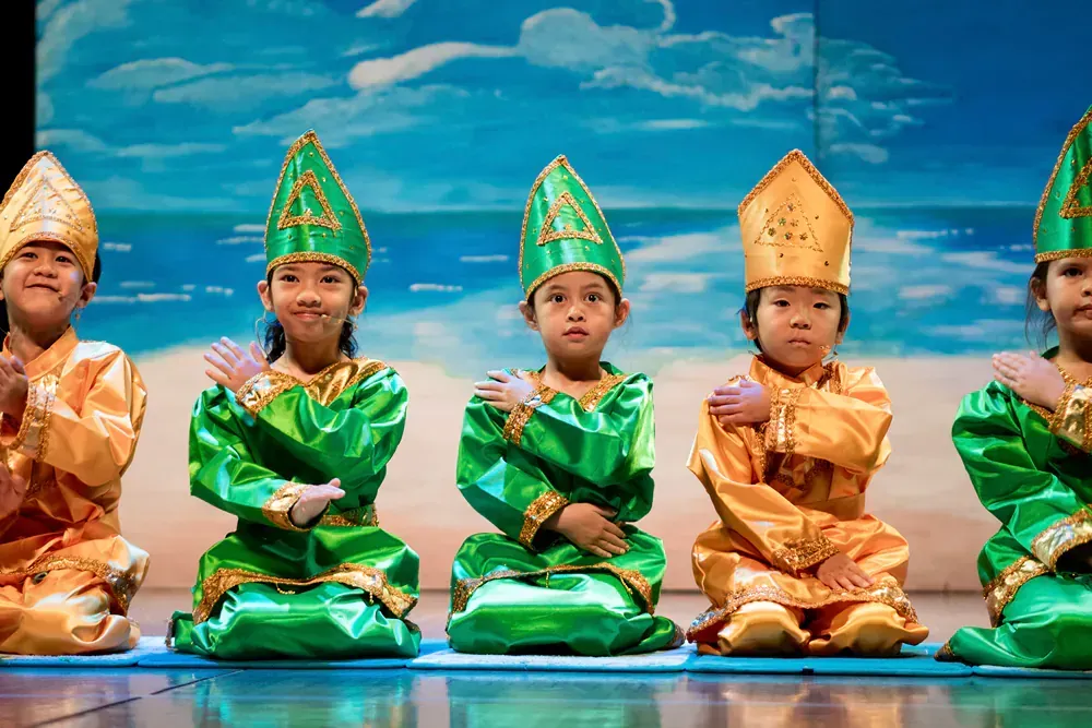 A group of children in traditional costumes are sitting on a stage.