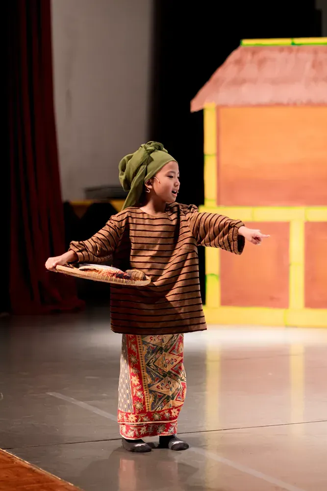 A little girl is standing on a stage holding a tray.
