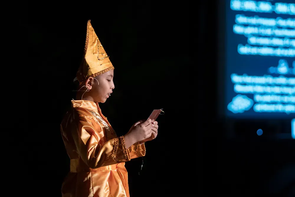 A young boy in a costume is looking at a cell phone in a dark room.