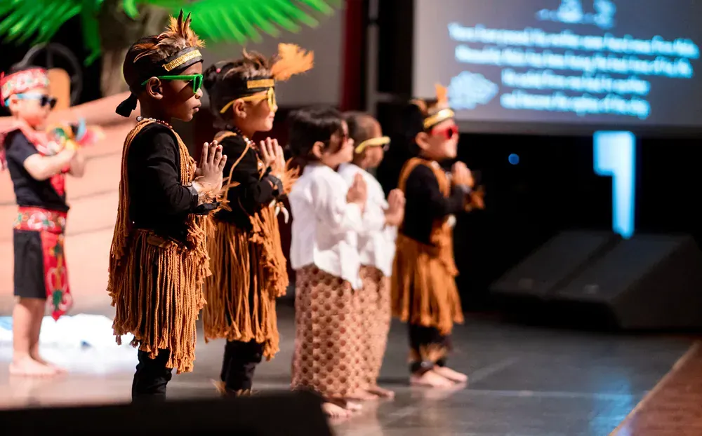 A group of children are standing on a stage wearing native american costumes.
