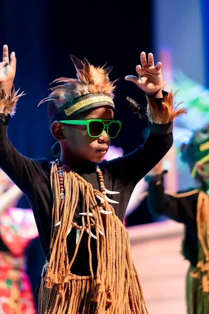 A young boy wearing sunglasses and a native american costume is dancing on a stage.
