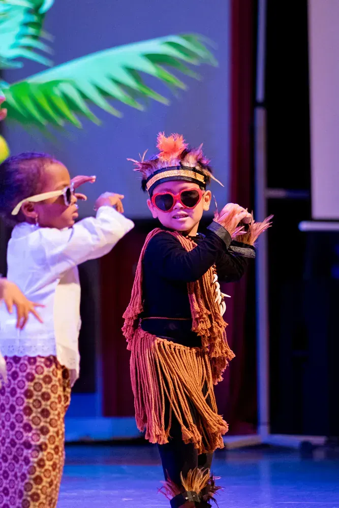 A group of children are dancing on a stage and one of them is wearing sunglasses.