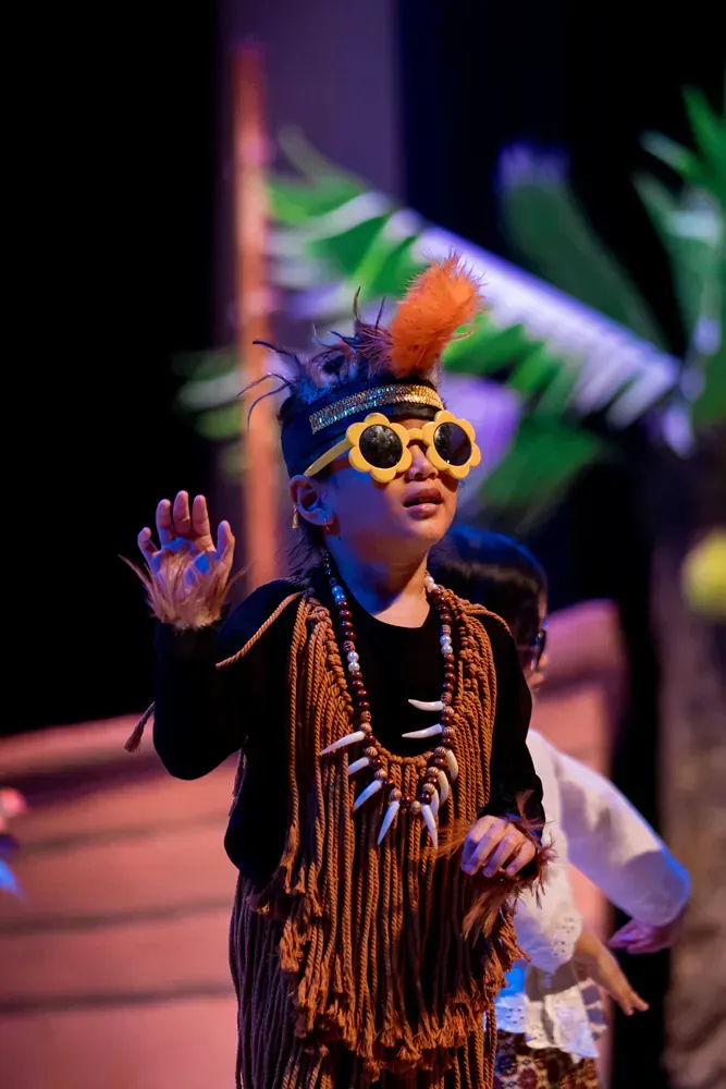 A young boy in a native american costume and sunglasses is standing on a stage.