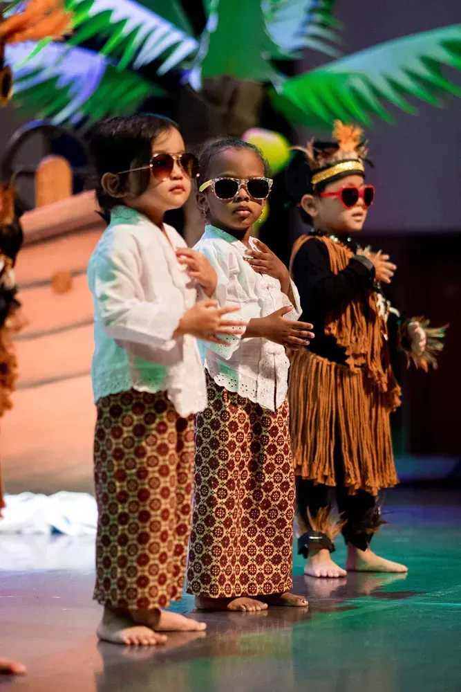 A group of young children wearing sunglasses and traditional costumes are standing on a stage.