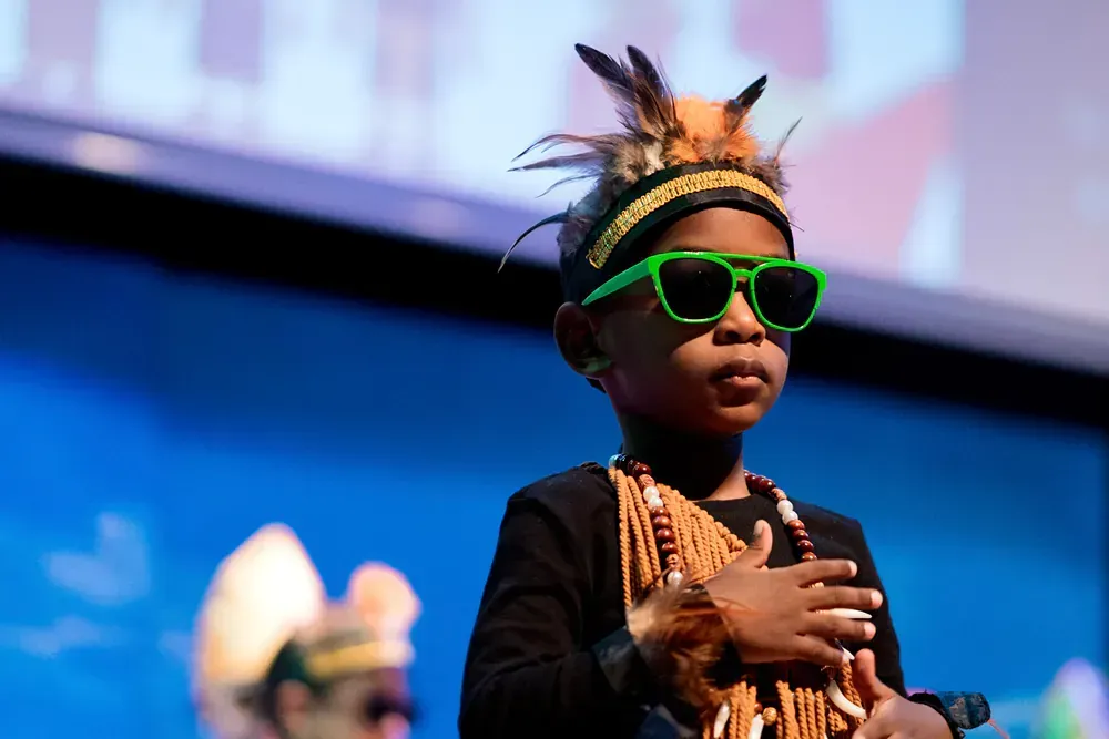 A young boy wearing green sunglasses and a feathered headband