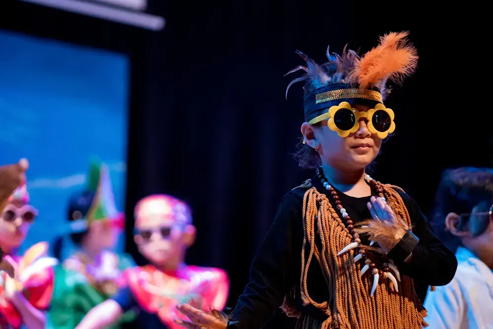 A boy in a native american costume is wearing sunglasses and feathers on his head.