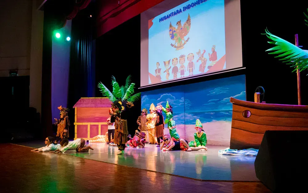 A group of people are dancing on a stage in front of a large screen.