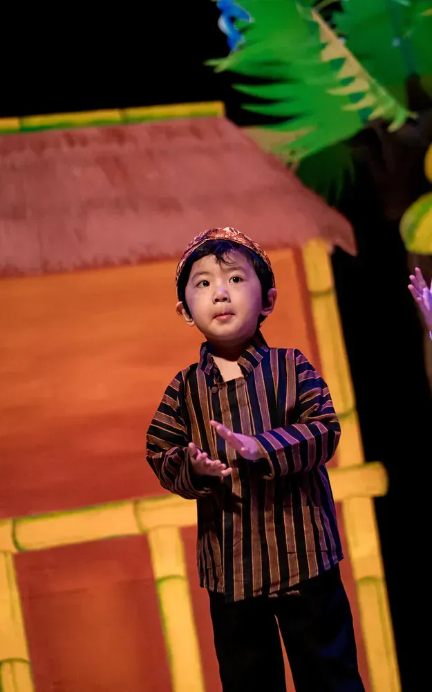 A young boy in a striped shirt and hat is standing on a stage.