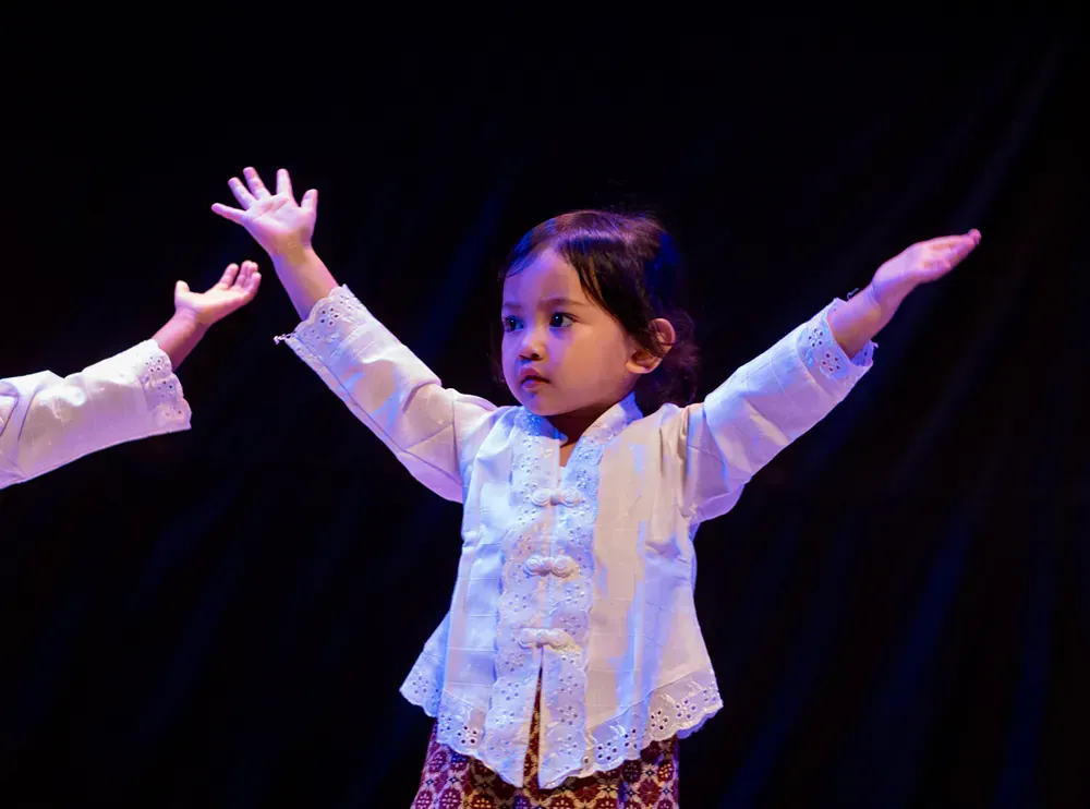 A little girl is standing on a stage with her arms outstretched.