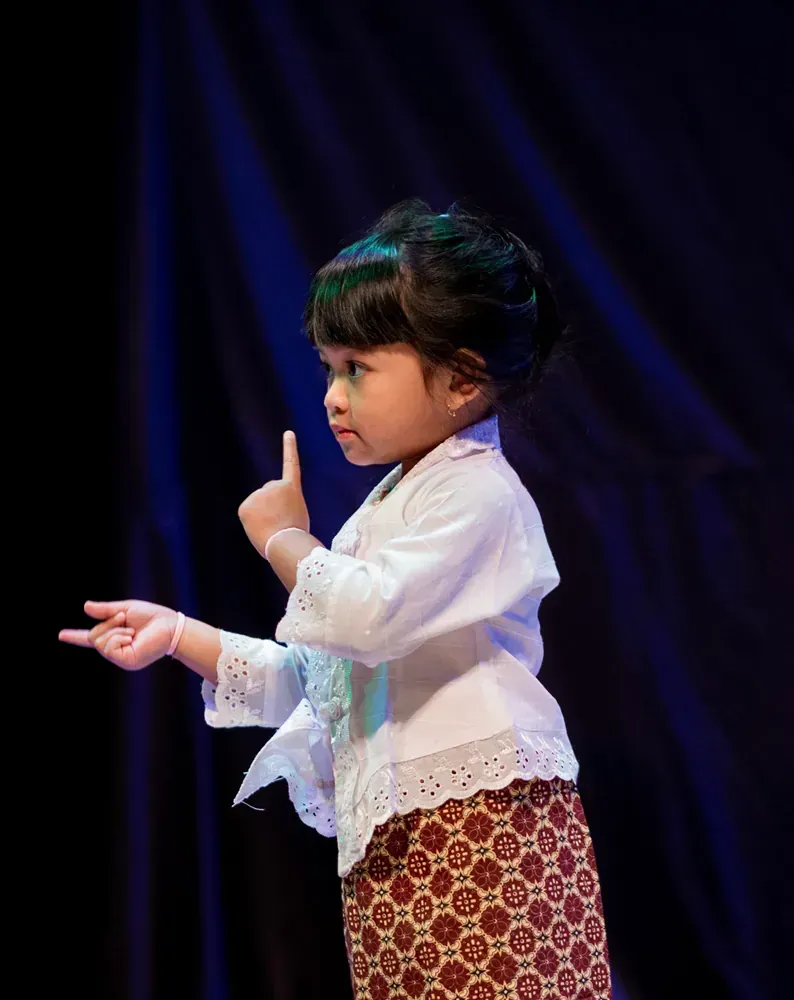 A little girl is giving a thumbs up on a stage.