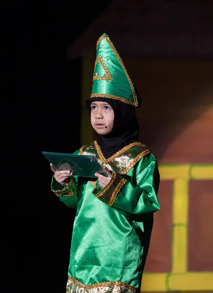 A little girl in a green costume is holding a piece of paper.