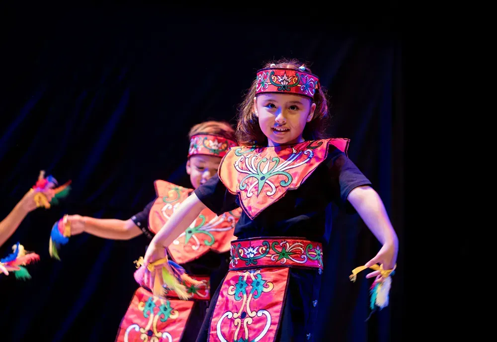 A group of children are dancing on a stage in traditional costumes.