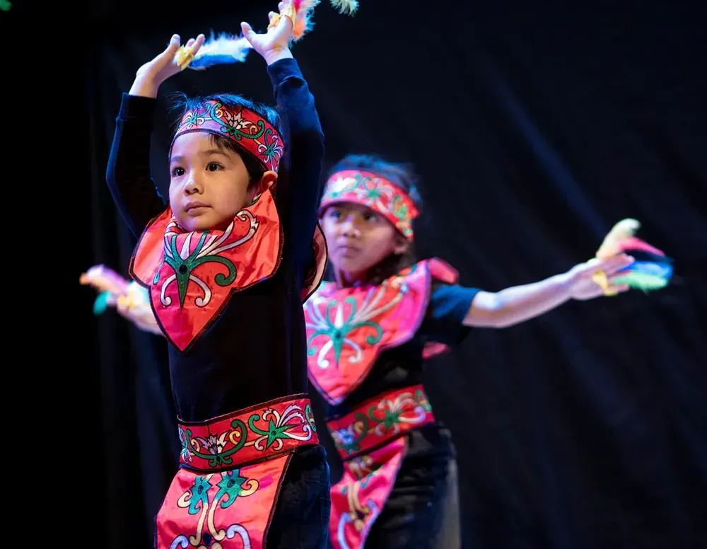Two young girls are dancing on a stage in traditional costumes.