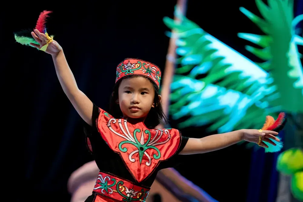 A little girl in a red and black outfit is dancing on a stage.