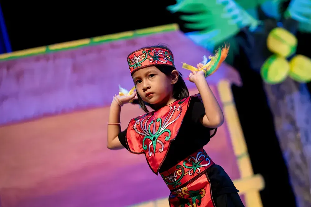 A little girl in a red and black costume is dancing on a stage.
